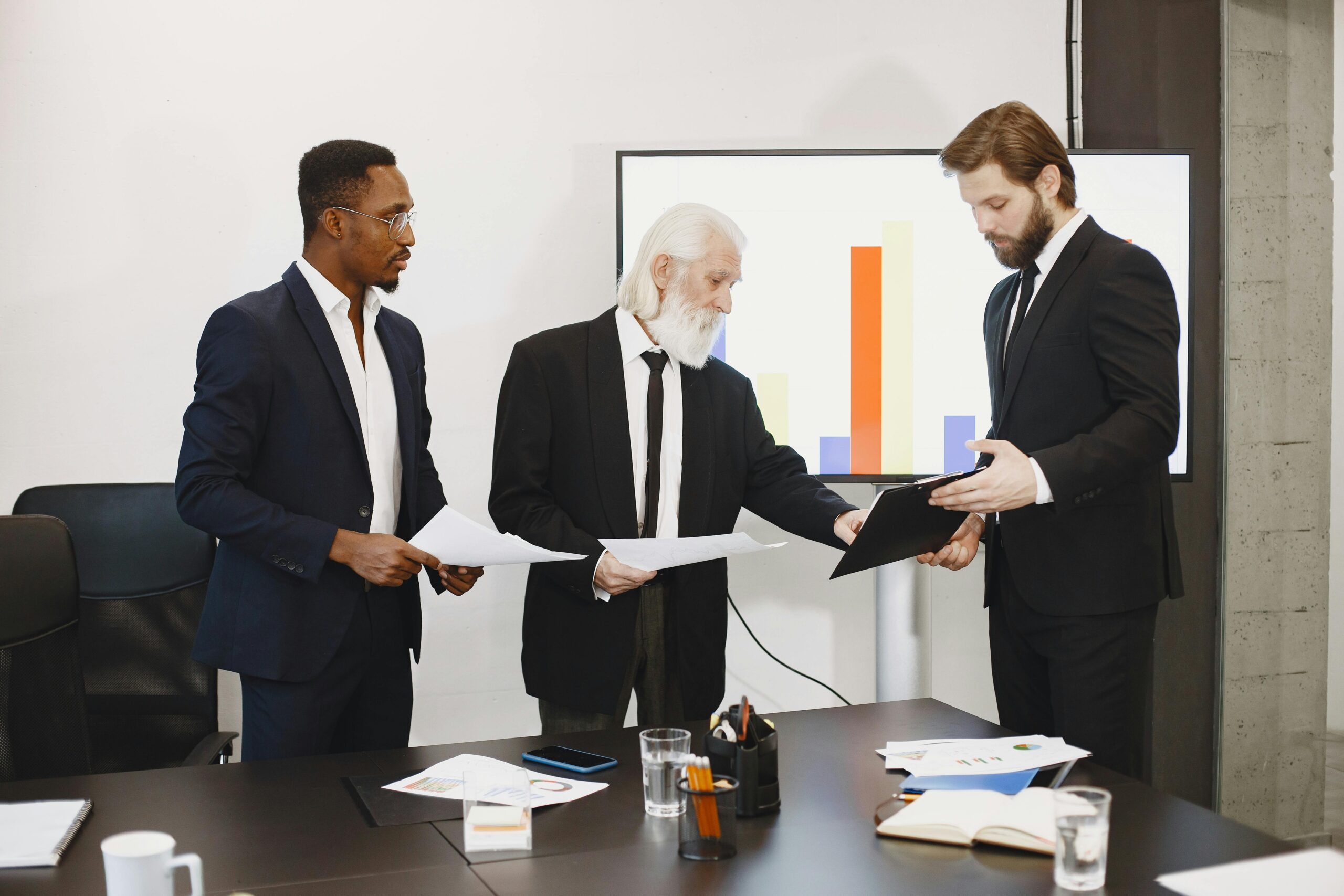 service-1 Three businessmen discussing documents in a conference setting with a presentation screen.